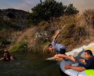 Eddie Lopez and his son, Eddie Jr. frolic near a drainage pipe along the San Gabriel River, in California, during the recent heat wave.  PHOTOGRAPH BY ROBERT GAUTHIER, LOS ANGELES TIMES/GETTY IMAGES