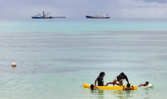 Children play in a small boat as large fishing boats sit offshore in Vanuatu. Photograph: Sean Gallagher/The Guardian